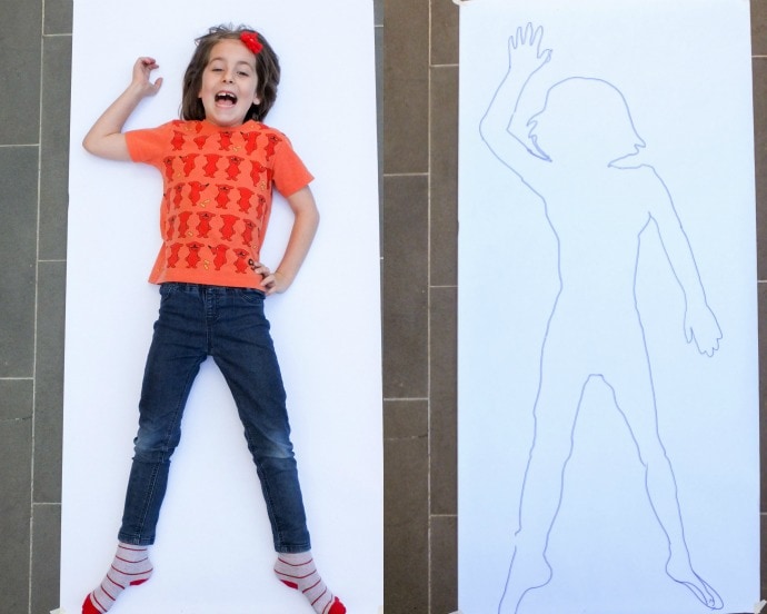 Child laying on a piece of paper to create a drawing of themselves