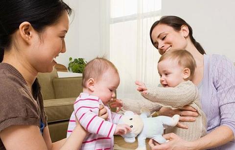 Two caregivers holding infants on laps, smiling and facing each other