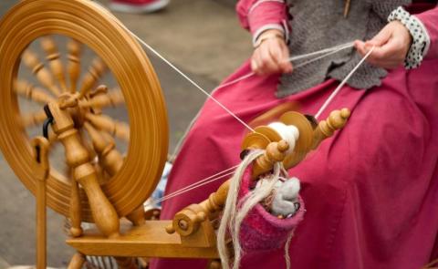 woman spinning fiber on an old fashioned spinning wheel