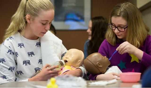 two tween girls holding baby dolls, practicing feeding the dolls.