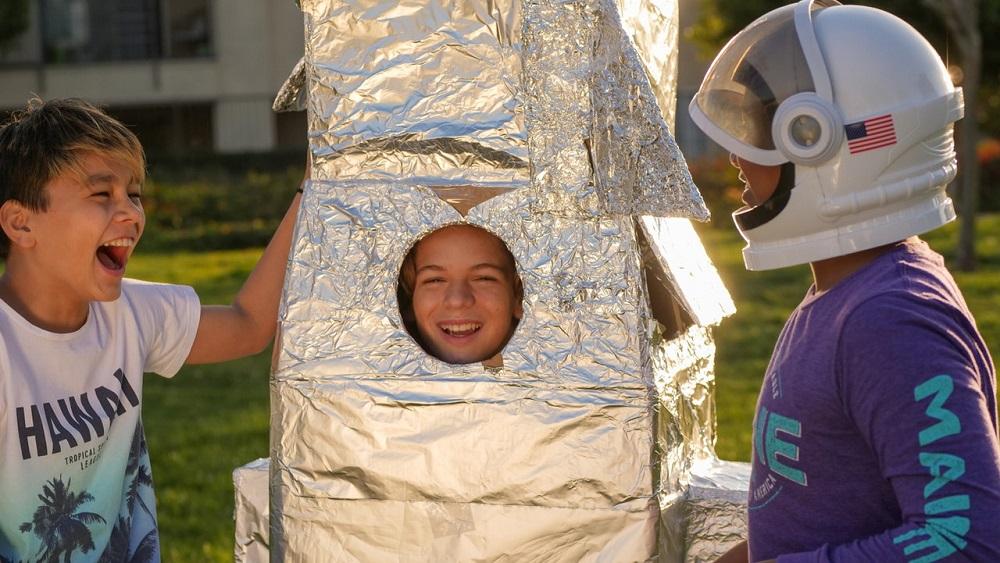 Boy inside a pretend rocket made with silver foil, with friends.