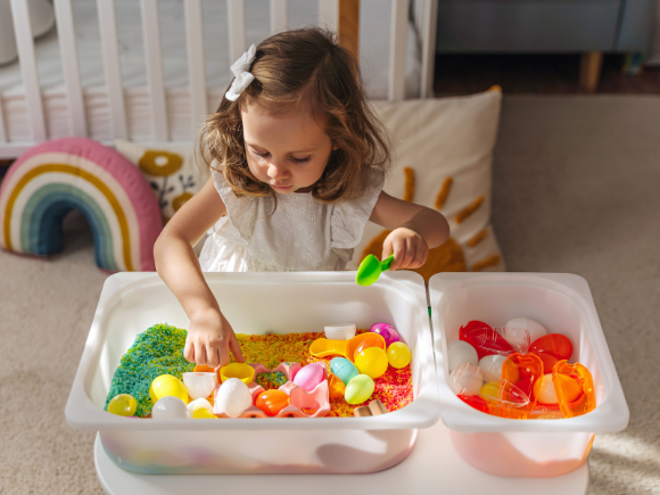 girl playing with tub of rice and toys